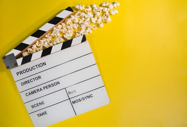 Clapperboard with popcorn pouring out of it on a yellow background